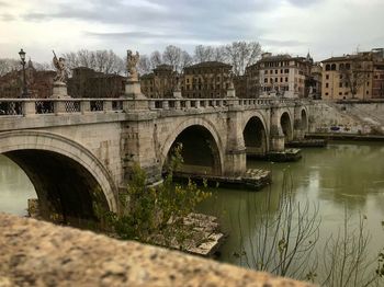 Arch bridge over river in city against sky