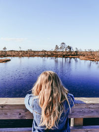 Rear view of little blonde girl in water against sky in bog