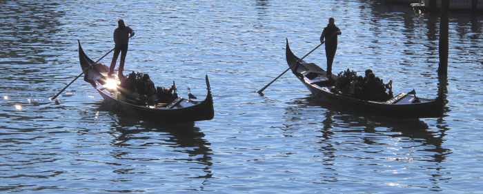 Silhouette people oaring gondolas on canal