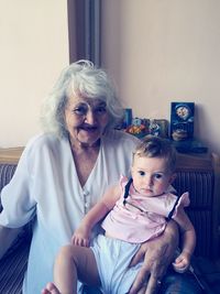 Portrait of smiling grandmother with baby girl sitting on soda