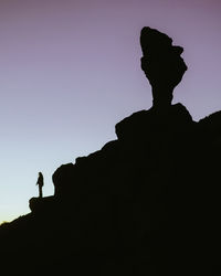 Silhouette of unrecognizable person standing on rocky hill in highlands on background of sundown sky