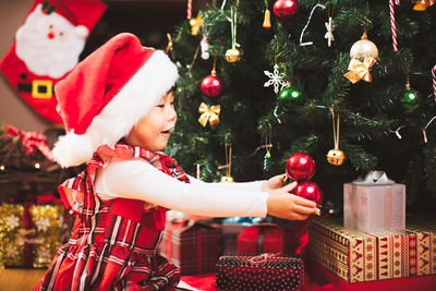 Smiling girl holding decoration by christmas tree