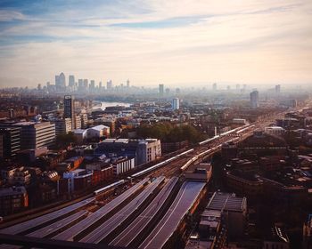 Aerial view of trains moving on railroad track by cityscape against cloudy sky