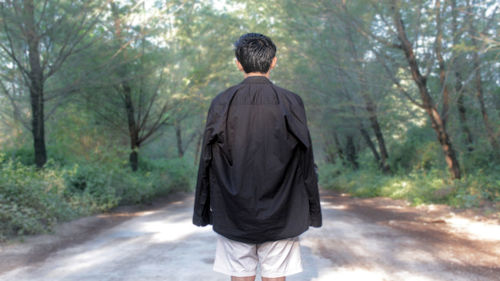 Rear view of young man standing on footpath amidst trees in forest