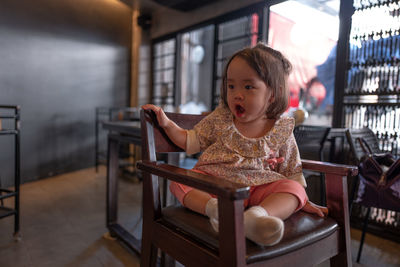 Thoughtful baby girl sitting on chair in restaurant