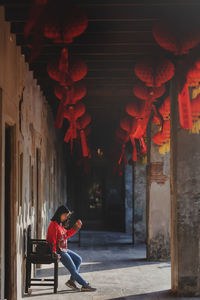 A lonely red dress girl sitting on a chinese wooden chair waiting for someone