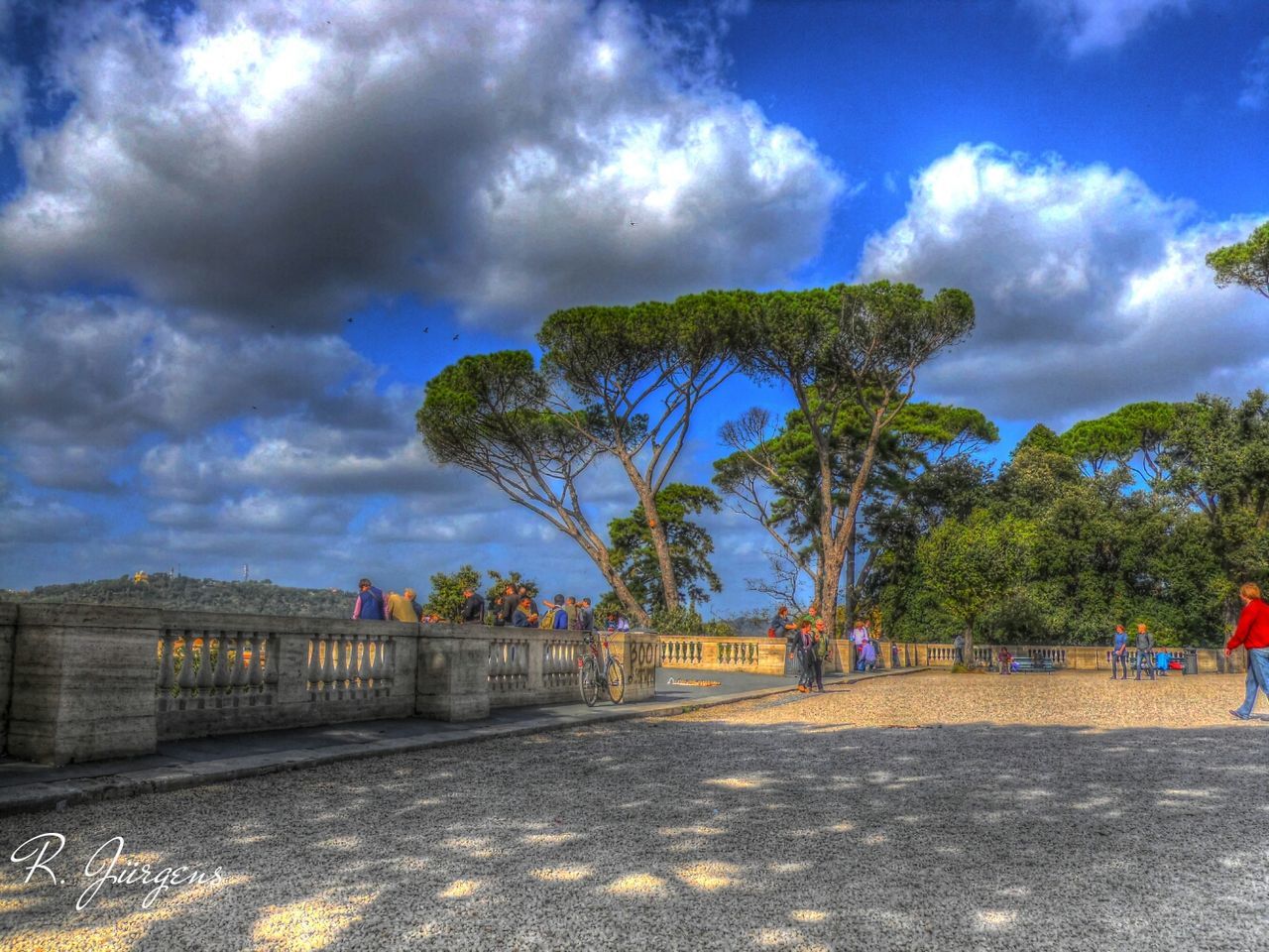 sky, tree, cloud - sky, cloud, cloudy, built structure, road, architecture, transportation, incidental people, railing, day, blue, street, nature, outdoors, building exterior, the way forward, sunlight, low angle view