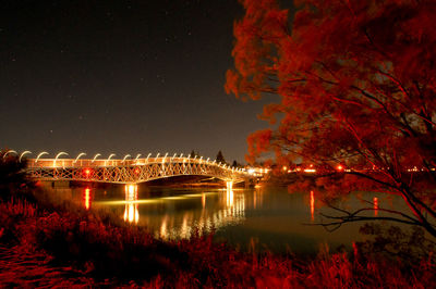 Illuminated bridge over river against sky at night