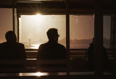 Men sitting against window during sunset