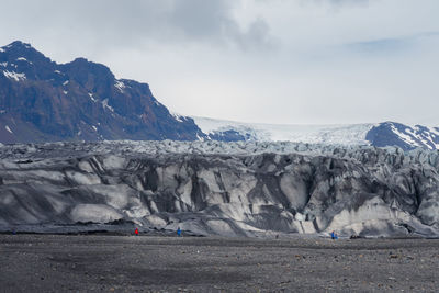 People in red and blue outdoor jackets dwarfed by a glacier on a cold day in southern iceland.