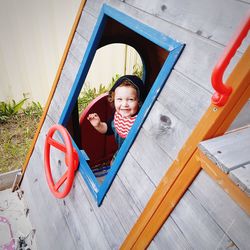High angle portrait of cheerful baby boy playing in playhouse at back yard