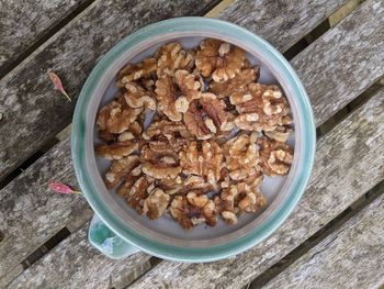 A bowl of walnuts viewed from above, lying on a wooden bench.