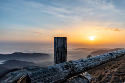 Wooden post on fog covered land against sky during sunset on mountain linzone