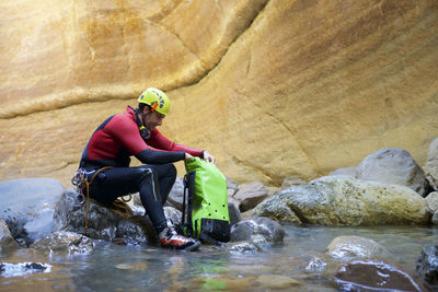 Side view of male hiker with backpack sitting on rocks in river