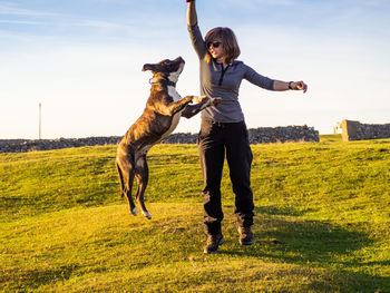 Full length of mature woman playing with dog on grass