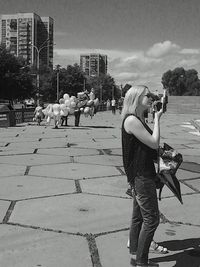 Rear view of woman playing with dog against sky in city