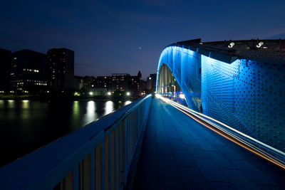 Illuminated footbridge over river in city at night