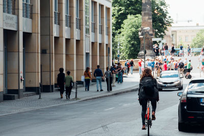 Rear view of woman riding bicycle on road by building