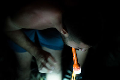 Man with flashlight bending on field at night