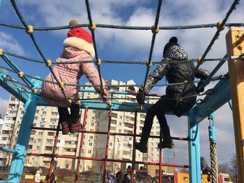 Low angle view of friends sitting ropes in playground