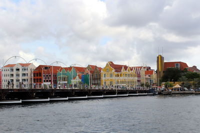 River by buildings in city against cloudy sky