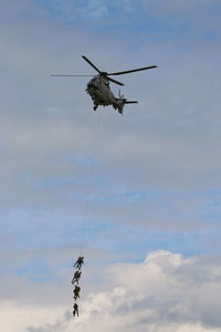 Army soldiers on rope hanging from helicopter against sky