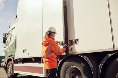 Female worker locking door of truck outside factory on sunny day