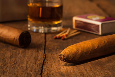 Close-up of cigars by whiskey glass on table