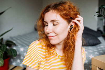 Happy red-haired girl listening music, at home in wireless headphones