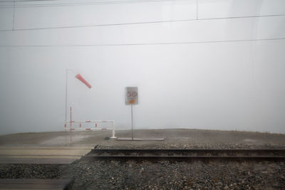 Road sign by railroad tracks against sky during winter