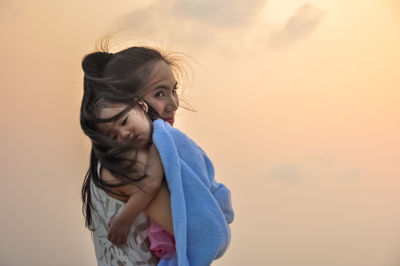 Portrait of mother carrying daughter against orange sky