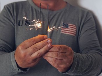 Midsection of man holding sparklers while standing against wall