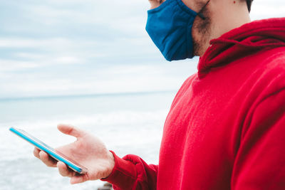 Midsection of man using mobile phone against sea