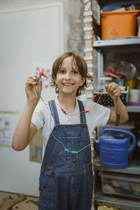 Portrait of smiling female student holding electric motor connected to wires at technology workshop in school