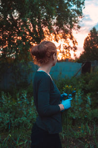 Side view of boy holding plant against trees