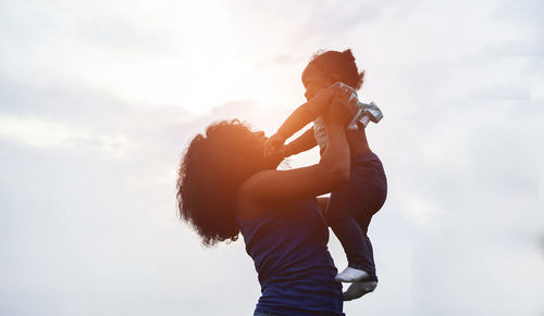 Low angle view of mother holding daughter against sky