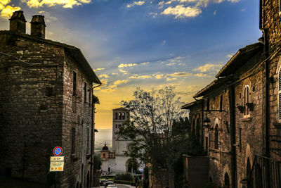 Road by buildings against sky during sunset