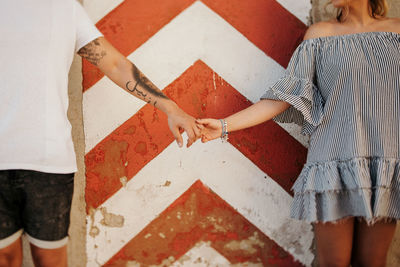 Unrecognizable young couple holding hands while standing against crumbling wall on city street