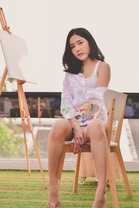 Portrait of woman sitting by canvas against sky