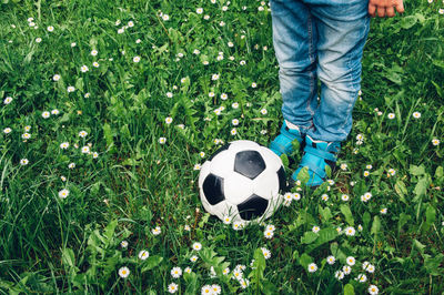Low section of boy standing by soccer ball on grassy field