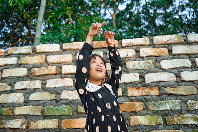 Portrait of smiling girl standing against brick wall