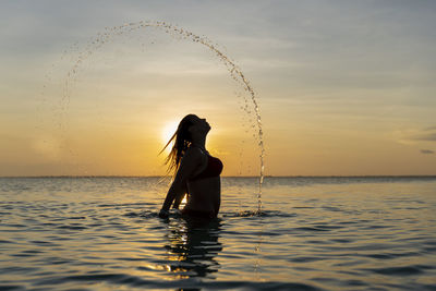 Woman in sea against sky during sunset