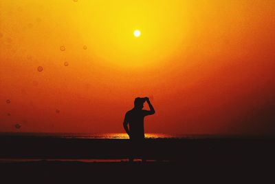 Silhouette man standing against orange sky during sunset