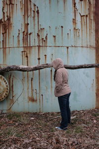 Full length of woman wearing hooded shirt against rusty water tank