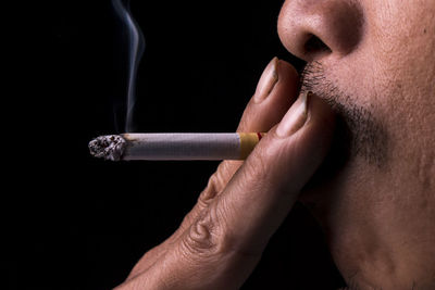 Cropped image of man smoking cigarette against black background