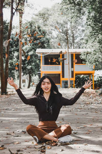 Portrait of smiling woman sitting on plant against trees