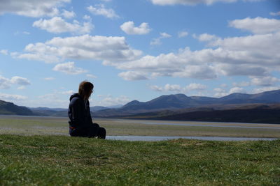 Man sitting on field by mountains against sky