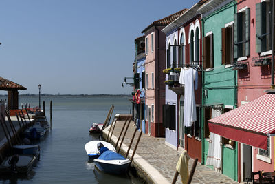 Boats moored in sea by houses against clear sky