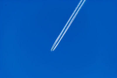 Low angle view of airplane with vapor trail against clear blue sky