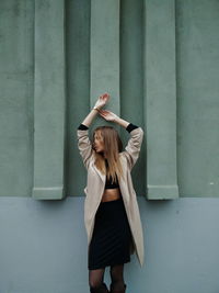 Fashionable woman looking away while standing against wall